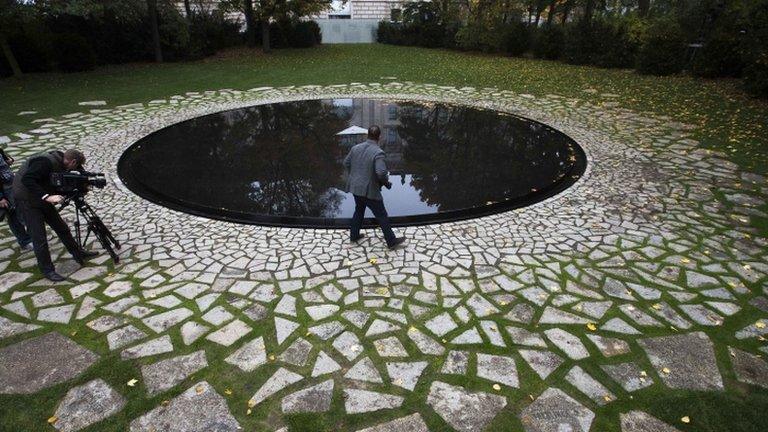 Media stand around a memorial to the Sinti and Roma murdered during Nazi rule near the Reichstag in Berlin