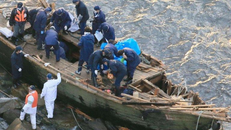 Police officers investigating a wooden boat with Korean language markings on Sado island, Niigata City, on 28 November 2012