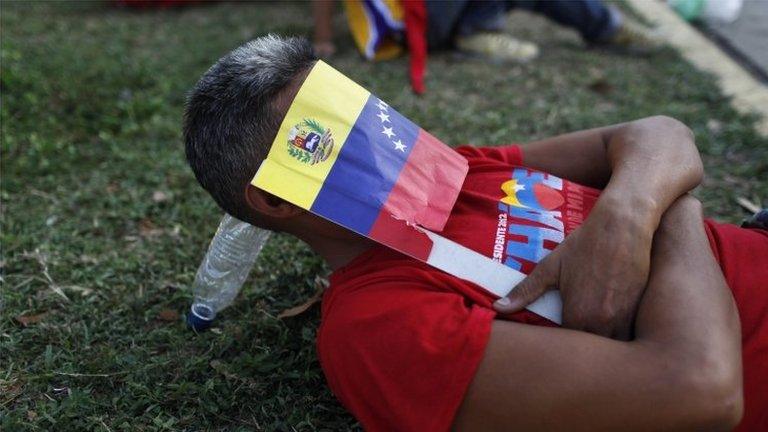 A Venezuelan man covers his face with a paper flag