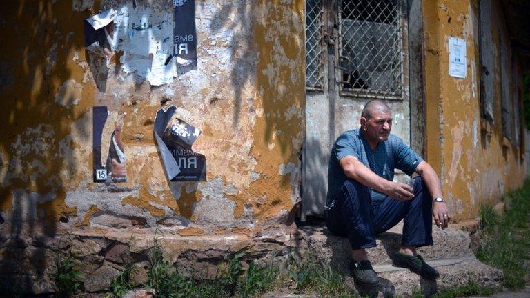 A man rests on a doorstep in a suburb of Sofia with torn election posters on a nearby wall, 13 May