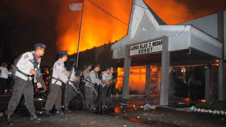 Armed Indonesian policemen secure the entrance of a burning prison compound in Medan city on July 11, 2013.