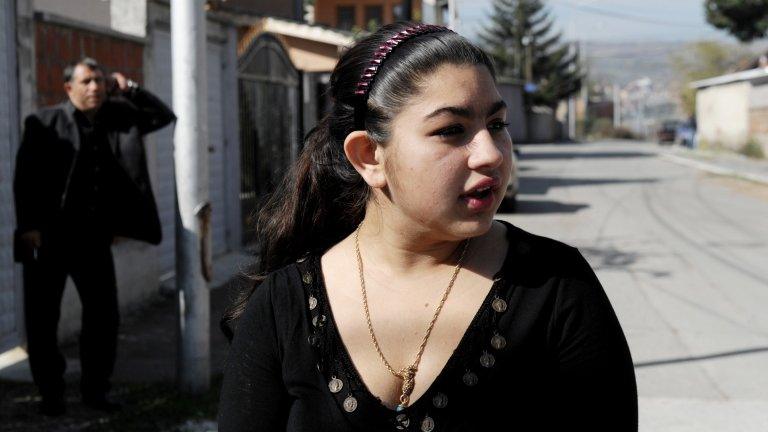 Leonarda Dibrani speaks to the media as her father Resat talks on his mobile phone outside their temporary home in Mitrovica