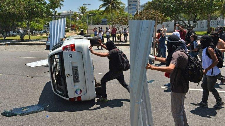 Protesters turn over a car during clashes in Barra da Tijuca on 21 October 2013