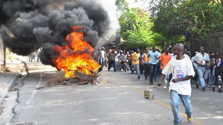 Protesters walk past a burning barricade in Port-au-Prince. Photo: 18 November 2013