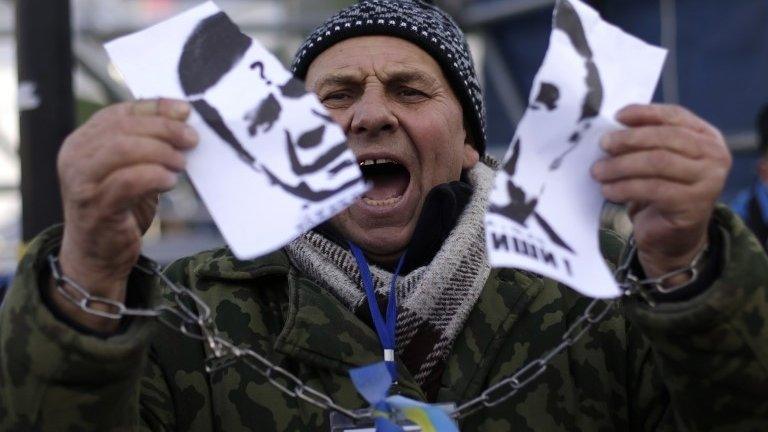 A protester in Kiev, with symbolically chained hands, rips up a picture of Ukrainian President Viktor Yanukovych, 29 November