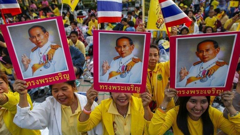 Well-wishers hold pictures of Thai King Bhumibol Adulyadej and wave Thai national flags as they gather to celebrate his 86th birthday near Klai Kangwon Palace, Hua Hin, Prachuap Khiri Khan province, 5 December 2013