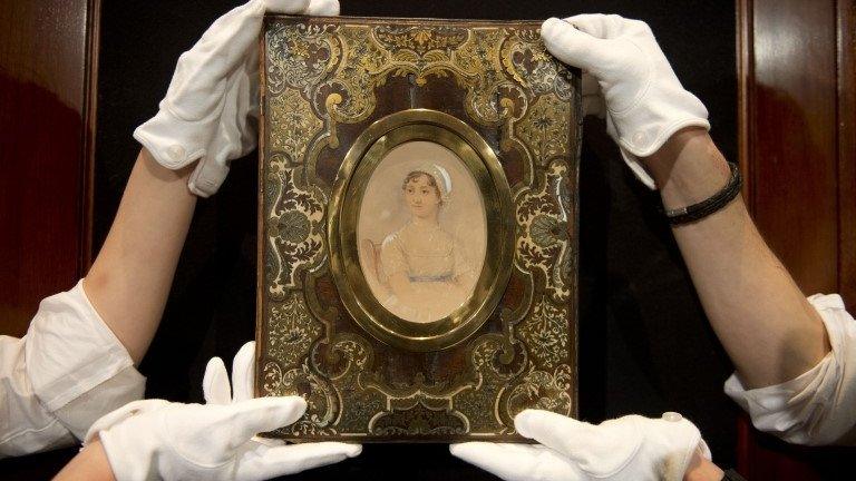 Two pairs of hands in white gloves hold up a portrait of Jane Austen