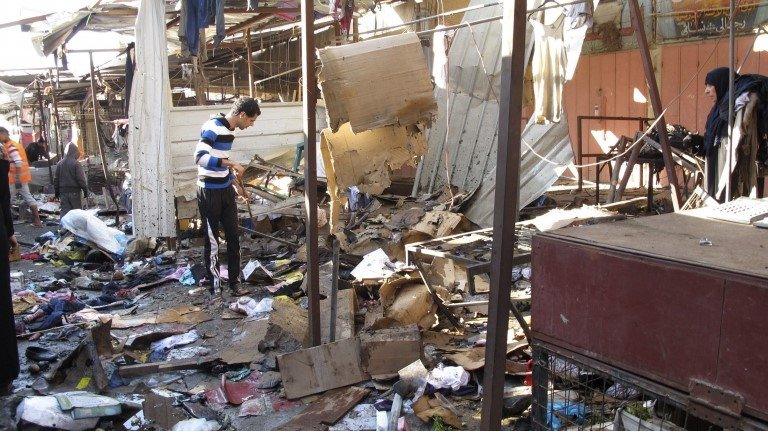 People stand among debris at the site of a bomb attack at a marketplace in Baghdad's Doura District December 25, 2013