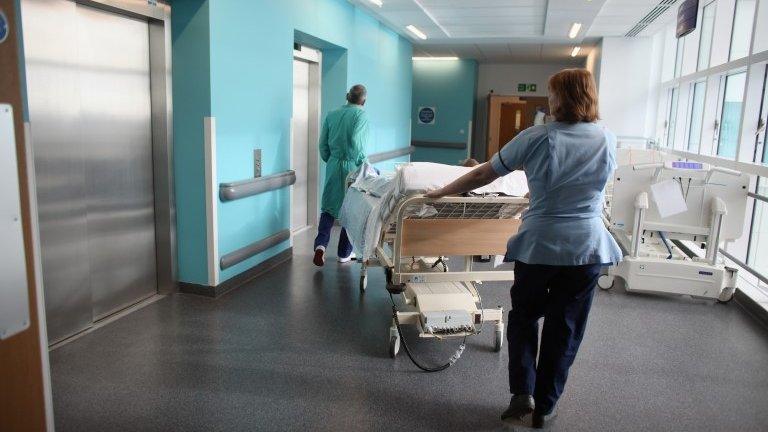 Two medical staff wheel a bed along a hospital corridor