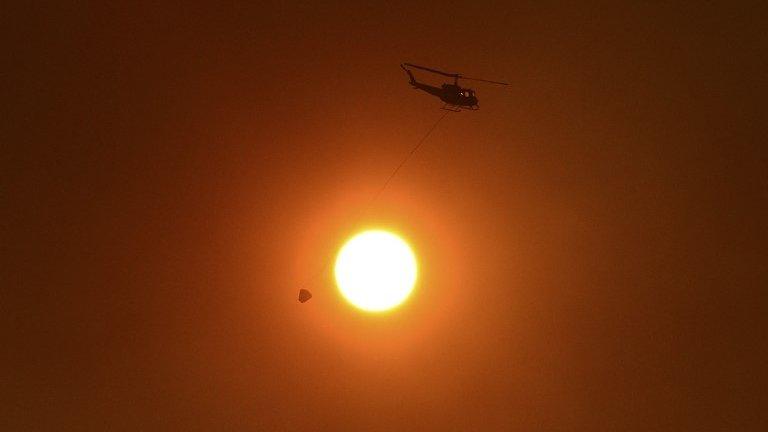 A helicopter with a bucket used for carrying water for dropping onto bushfires, flies past the sun as it is obscured by smoke in western Sydney 20 October 2013