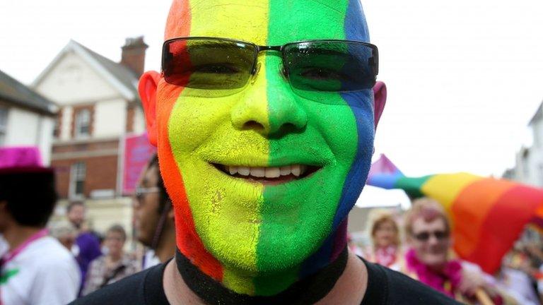 A man with his face painted in multi-coloured stripes on a Gay Pride march