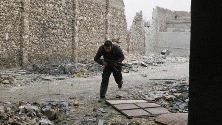 A man carrying a gun runs along a wrecked street