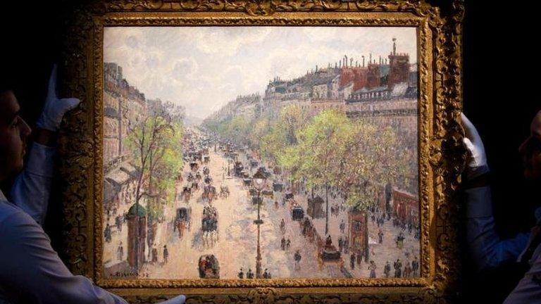 Sotheby's employees hold up Camille Pissarro's Le Boulevard Montmartre, matinee de printemps (1897)