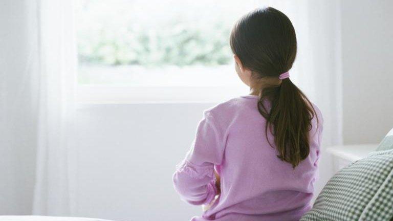 A child sits on a bed with her back to the camera