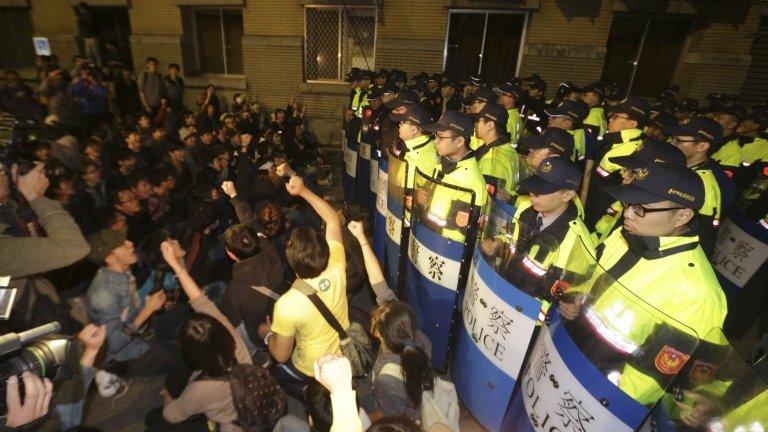 Policemen in riot gear keep guard as demonstrators shout slogans to protest against a trade pact with mainland China, near Taiwan's government headquarters in Taipei, on 23 March 2014