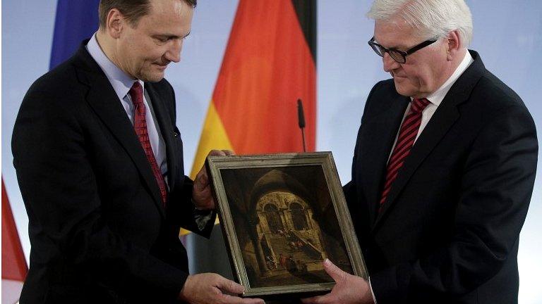 German Foreign Minister Frank-Walter Steinmeier (R) passes the "Palace Stairs" painting to his Polish counterpart from Radoslaw Sikorski