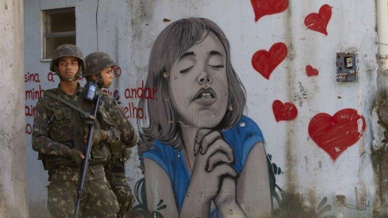 Brazilian soldiers stand next to a graffiti during an operation to occupy the Mare slum complex in Rio de Janeiro, 5 April