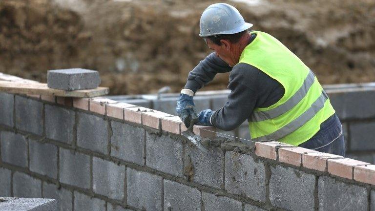 A builder adding bricks to the wall of a house which is being built