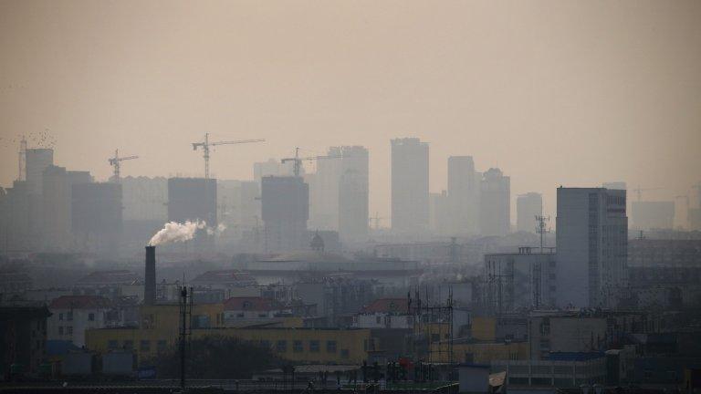 Smoke rises from a chimney among houses as new high-rise residential buildings are seen under construction on a hazy day in Tangshan, Hebei province, on 18 February 2014