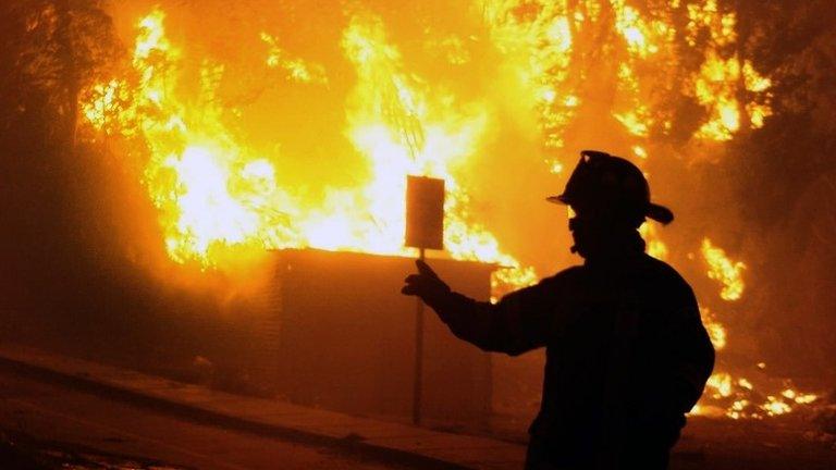 A firefighter stands next to burning houses during a fire in Valparaiso, 110 km west of Santiago, Chile, on 12 April 12, 2014.