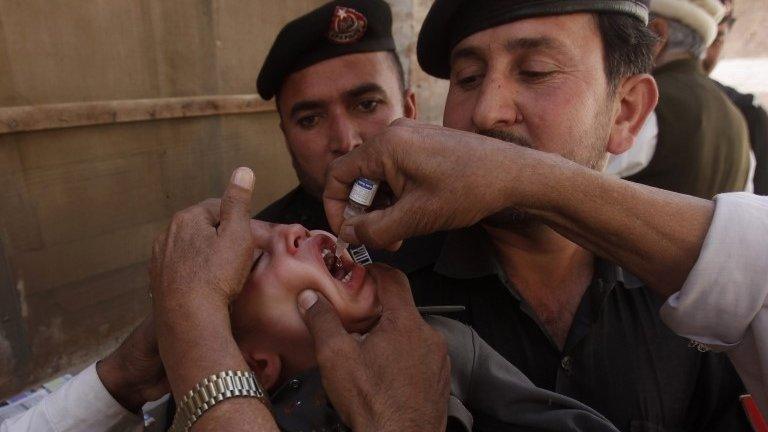 Polio workers give polio vaccine drops to a child as police stand guard during a vaccination campaign in Peshawar, the capital of Khyber-Pakhtunkhwa province March 30, 2014