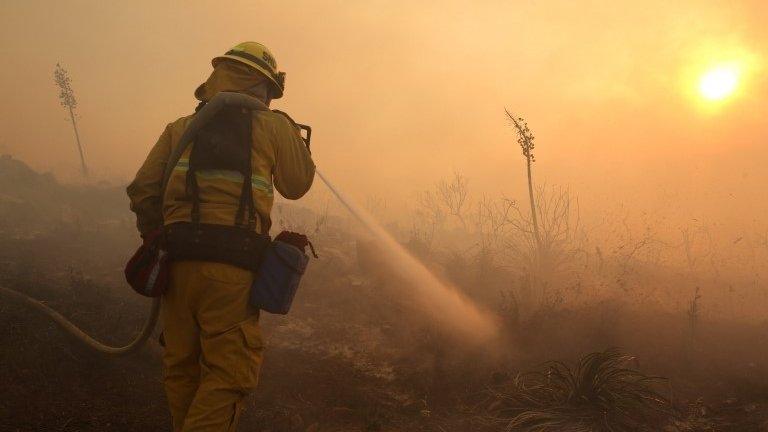 A firefighter puts down hot spots in front of a house in the hills in San Marcos, California, 1 May 2014
