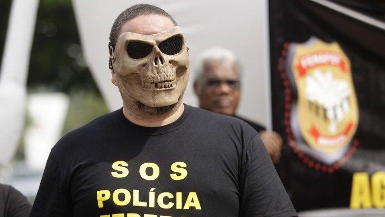 A federal police officer wears a skull mask and a T-shirt that reads in Portuguese "SOS Federal Police. Restructuring now!" during a police protest in Rio de Janeiro on 7 May, 2014