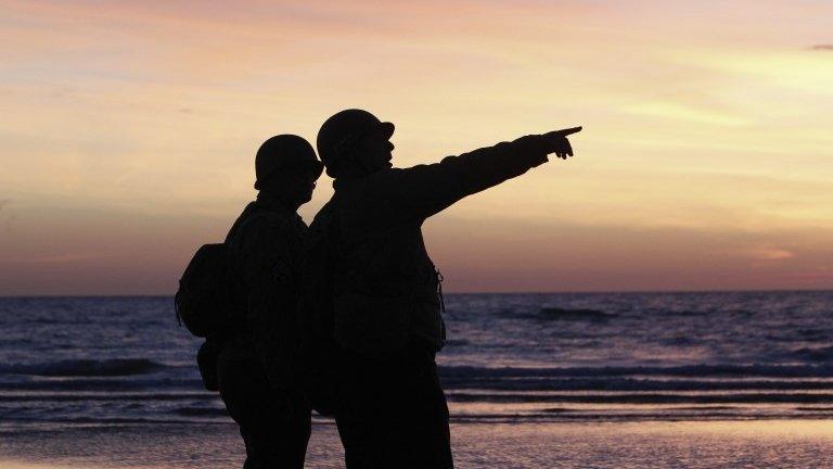 Two soldiers in silhouette, seen on a beach