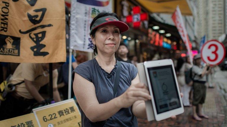 A pro-democracy activist holds a tablet showing an app to vote online outside a polling station in Hong Kong on 22 June 2014