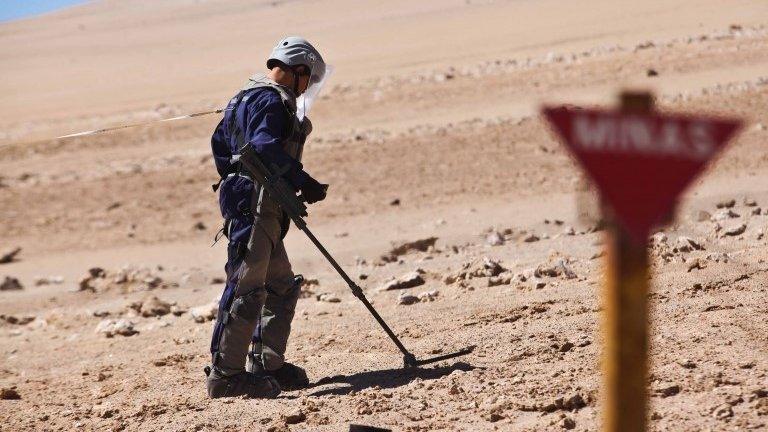 A Chilean army engineers wearing protective gear uses a magnetic detector in a minefield on 26 May 2014