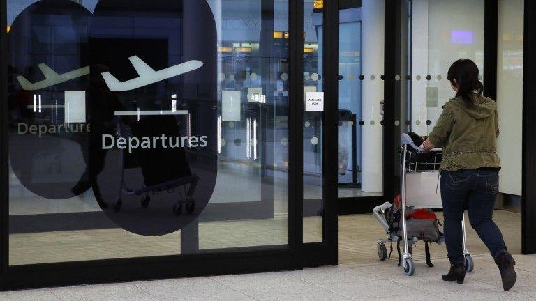 A woman walks through an airport, pushing a trolley