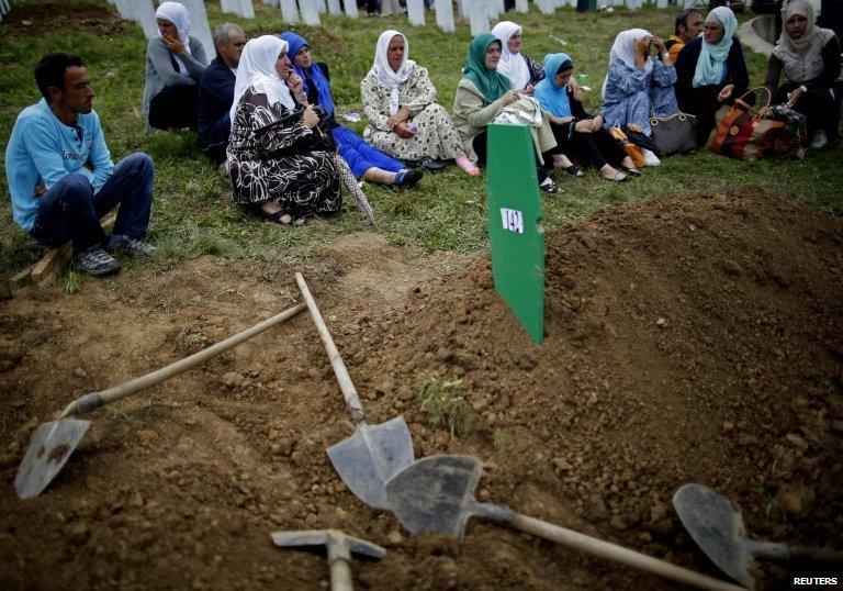 Bosnian Muslims sit near a grave after the mass funeral of 175 newly identified victims from the 1995 Srebrenica massacre, in Potocari Memorial Center, near Srebrenica, on 11 July 2014.