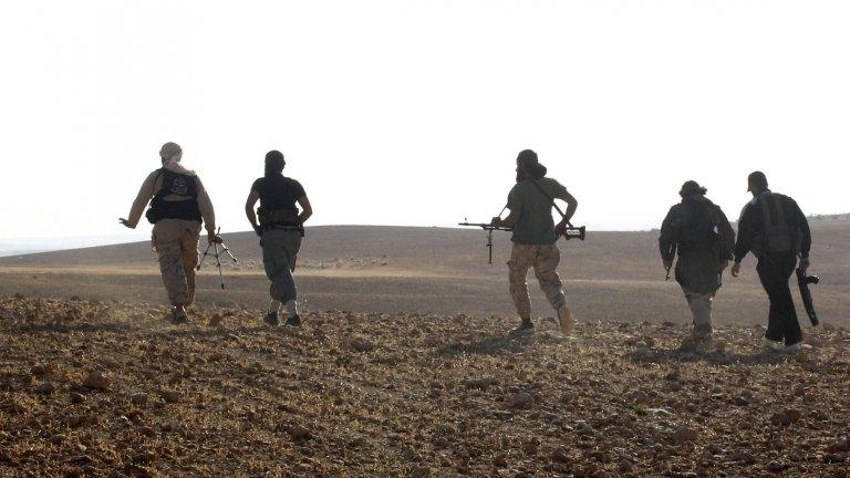 Free Syrian Army fighters walk with their weapons in Hama countryside on 3 June 2014