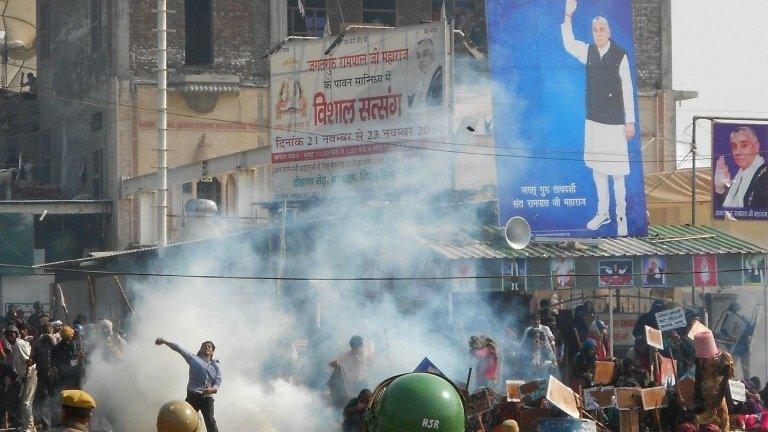 Indian security officials look on as an activist throws a stone in Hisar some 175kms north of New Delhi on November 18, 2014, during a confrontation between supporters of controversial guru Rampal Maharaj and security forces.