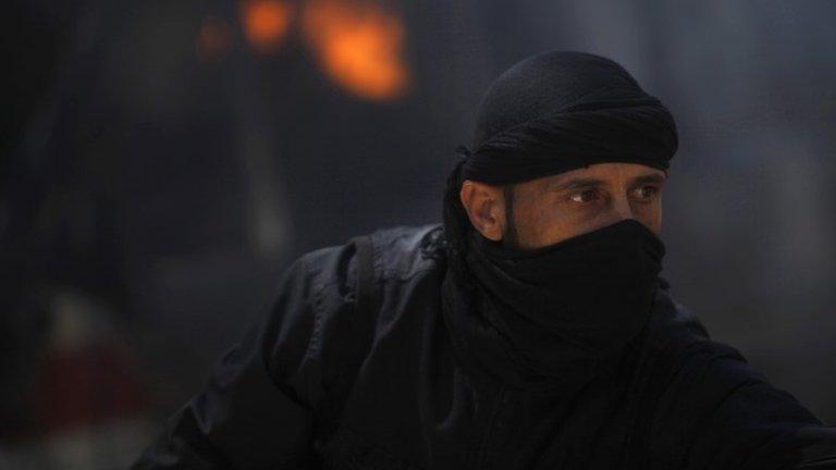 Member of the al-Nusra Front, al-Qaeda's affiliate in Syria, in front of a burning vehicle in Raqqa province (12 May 2013)