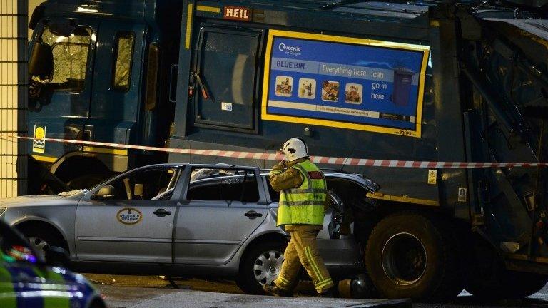 A firefighters walks close to a crashed bin lorry and a damaged car