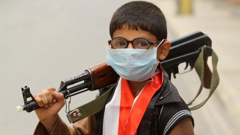 A boy wearing a surgical mask holds a weapon in Sanaa 3 April, 2015