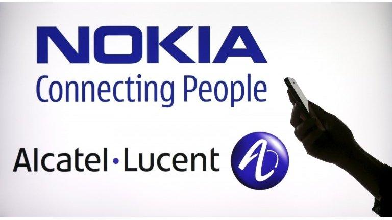 A woman holds a smartphone in front of a screen displaying both Nokia and Alcatel Lucent logos