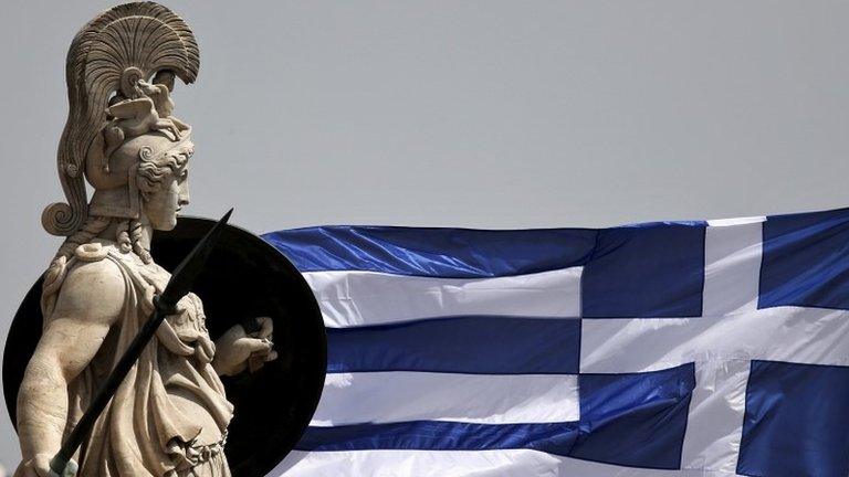 A Greek national flag flutters next to a statue of ancient Greek goddess Athena, in Athen