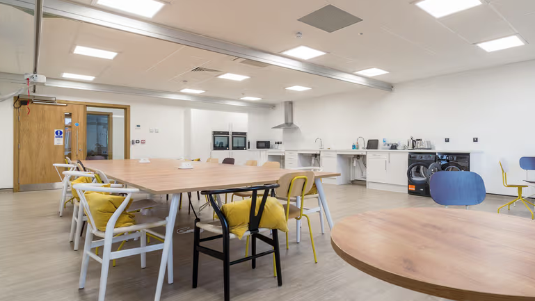 The Point facility at The Oaks Specialist College in Tonbridge. The kitchen space  features adaptable working spaces which can be seen in the image alongside a long table with chairs. 