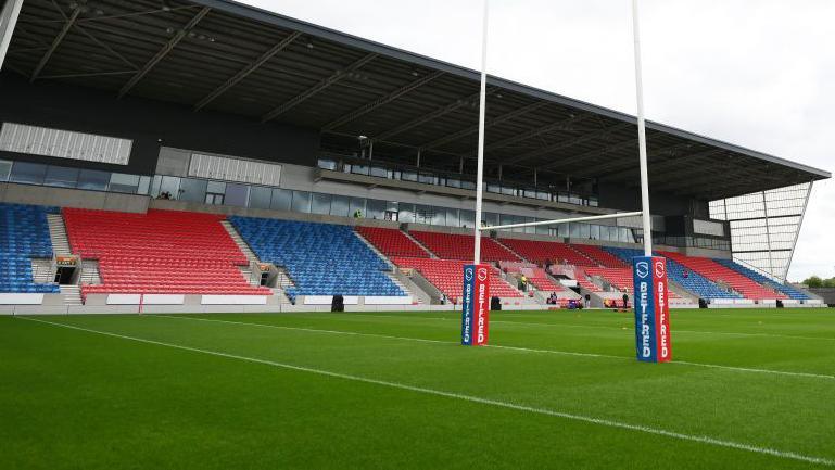 Rugby posts on a pitch with a stand at the Salford Community Stadium in the background