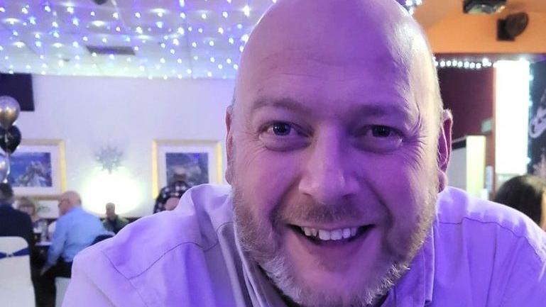 Kevin Rylance, 49, who has a bald head and a short beard, smiles at the camera