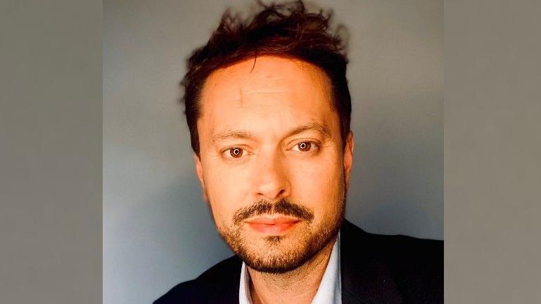 Portrait image of Janne Jarvis who is looking at the camera with a light smile. He has short brown hair and is wearing a black suit jacket and a white shirt underneath.
