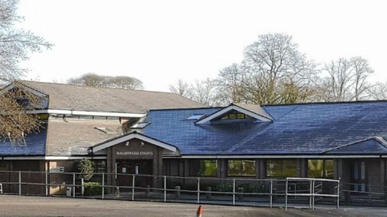 Truro Magistrates court. A two story building with a sloped roof. The windows are felecting the trees. There are trees in the background. The entrance to the court is visible