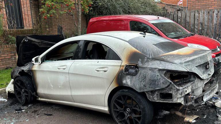 Side profile of a white Mercedes CLA, with extensive burn damage at the back and the front