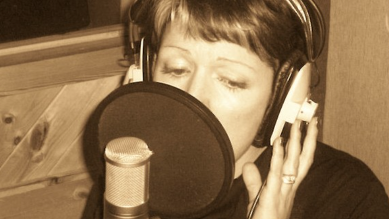 Lianne in a studio singing in front of a professional microphone. She has short hair and the picture is in sepia tones. 