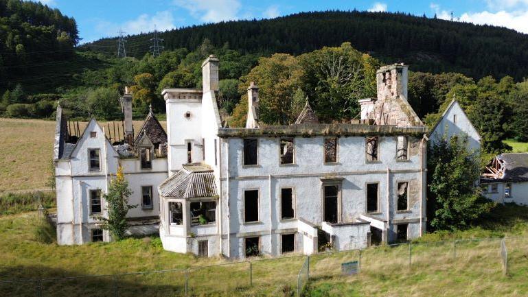 The ruins of historic Dunain House, with only exterior walls surviving from a fire. There are trees behind the property.