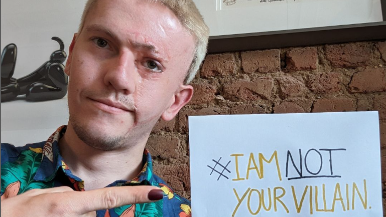 Actor Robert Rhodes holds a sign reading 'I am not your villain'