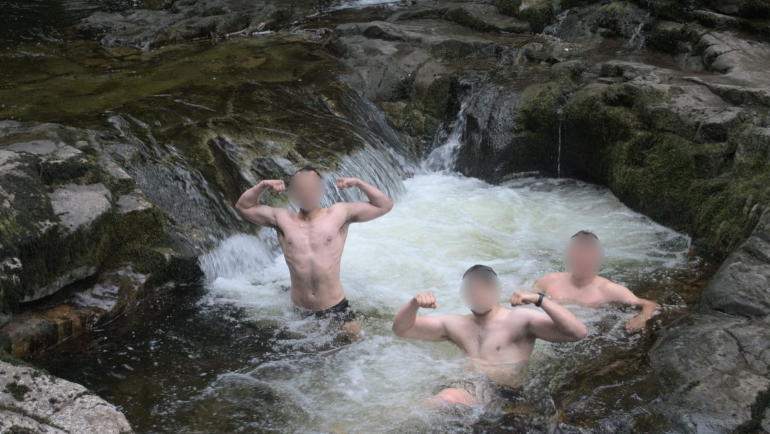 Three Active Club members pose, wearing only shorts, in a mountainside rock pool