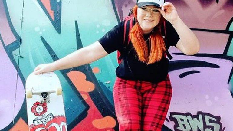 Woman poses with skateboard next to graffiti wall